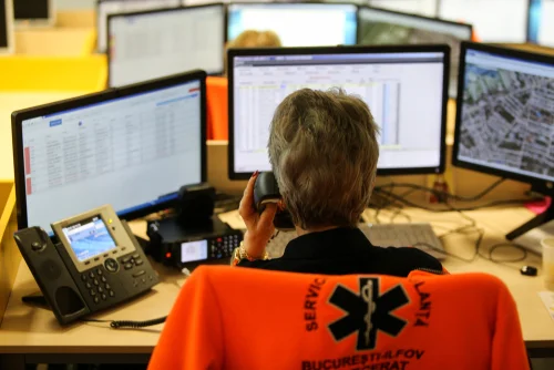 A dispatcher at a multi-monitor PSAP console takes a 911 call.